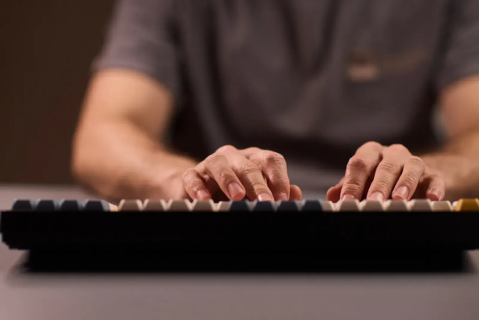 Deux mains posées sur un clavier mécanique noir, en train de taper, dans une lumière chaude et tamisée