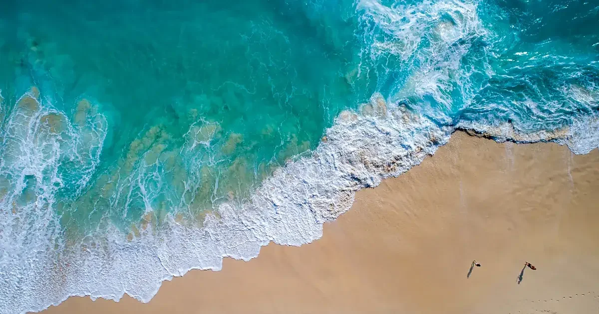 Littoral vu du ciel : l'eau passe du bleu profond au turquoise clair au-dessus d'un banc de sable doré