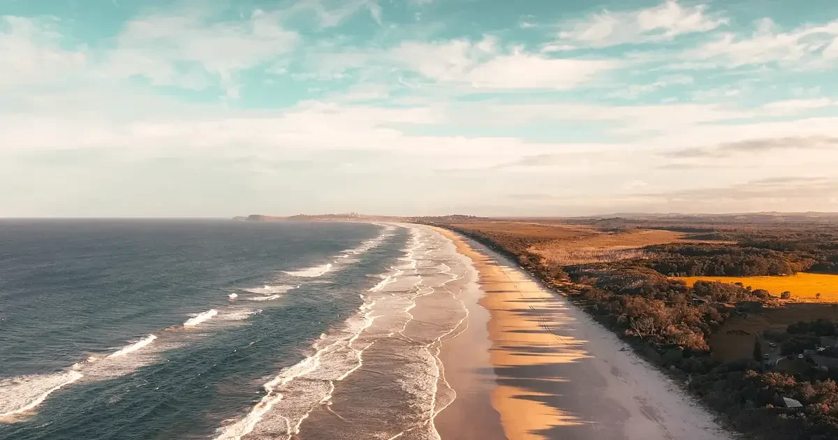 Longue plage vue du ciel, trains de houle parallèles arrivant sur le sable dans la brume du matin