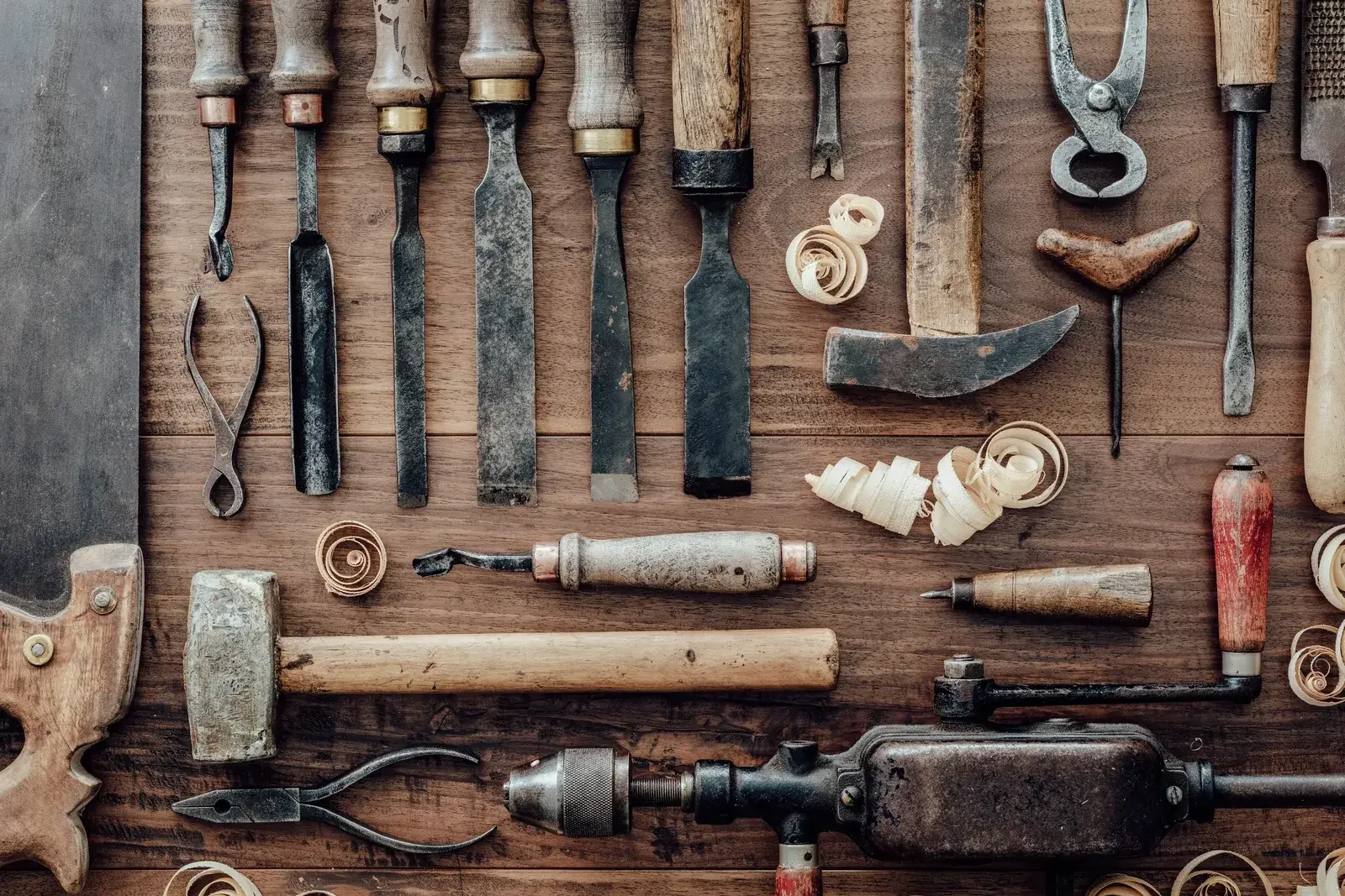Ciseaux à bois, maillet, vilebrequin et outils anciens alignés sur un établi en bois, vus de dessus